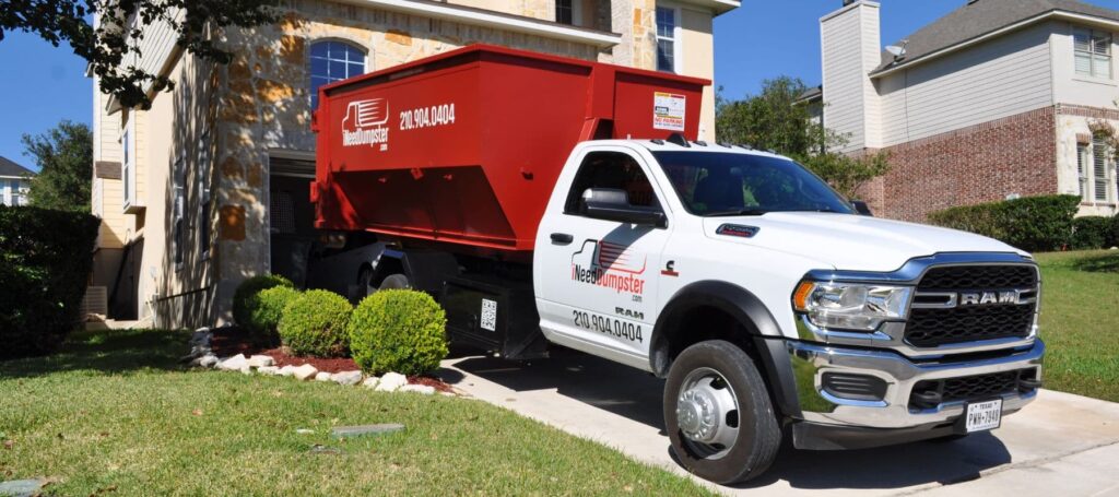 I Need Dumpster red dumpster sitting on a white company trust sitting outside of a home in san antonio on the driveway